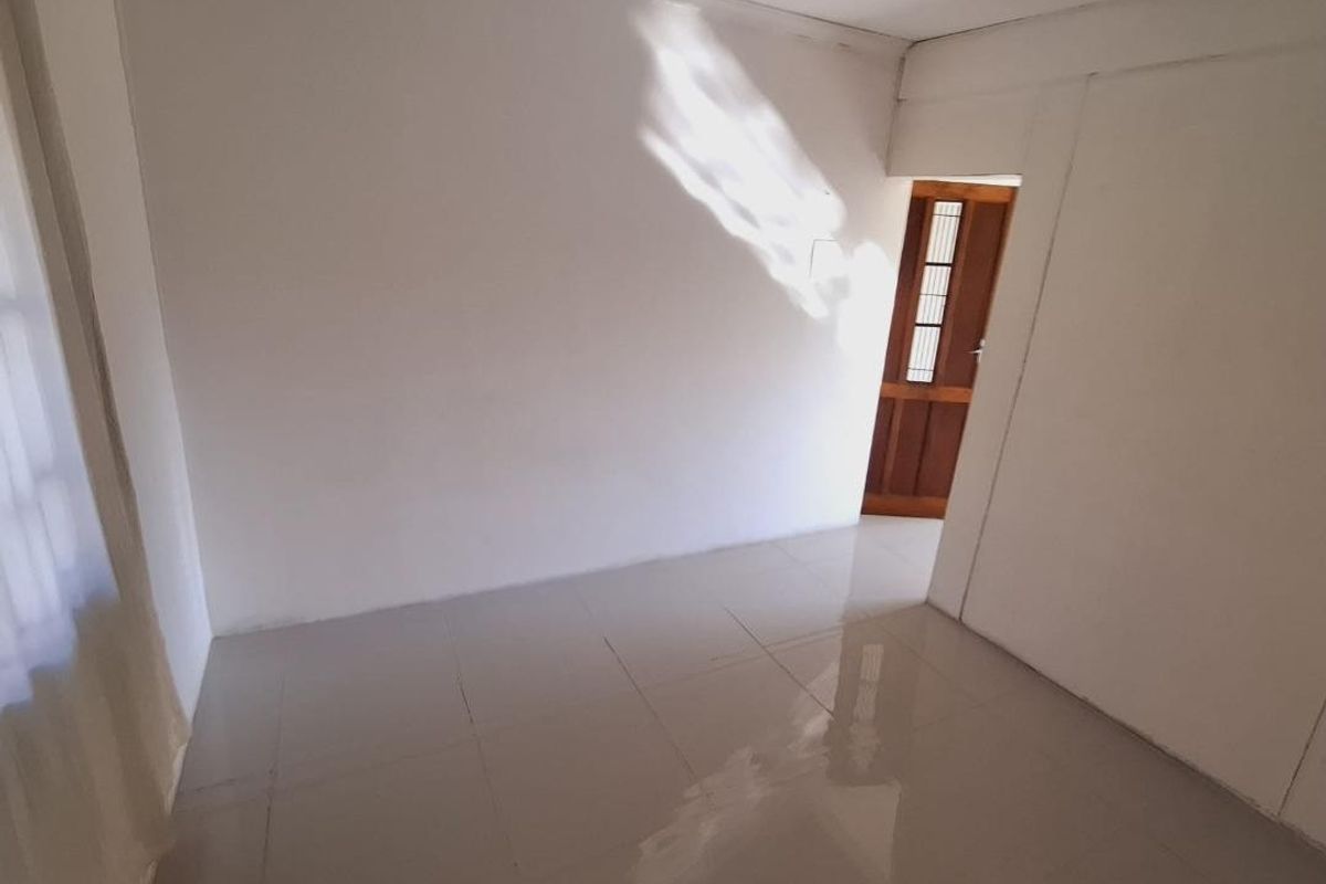 An empty bedroom featuring neutral tiled flooring and a wooden door, providing a blank canvas for personalization.