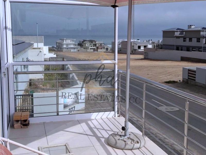A modern balcony featuring a stainless steel balustrade, glass enclosure, and tiled flooring, offering an elevated view of the surrounding neighborhood and coastline.