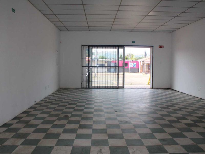 An empty open-plan retail space featuring a suspended ceiling, checkered flooring, and a secure metal entrance gate.