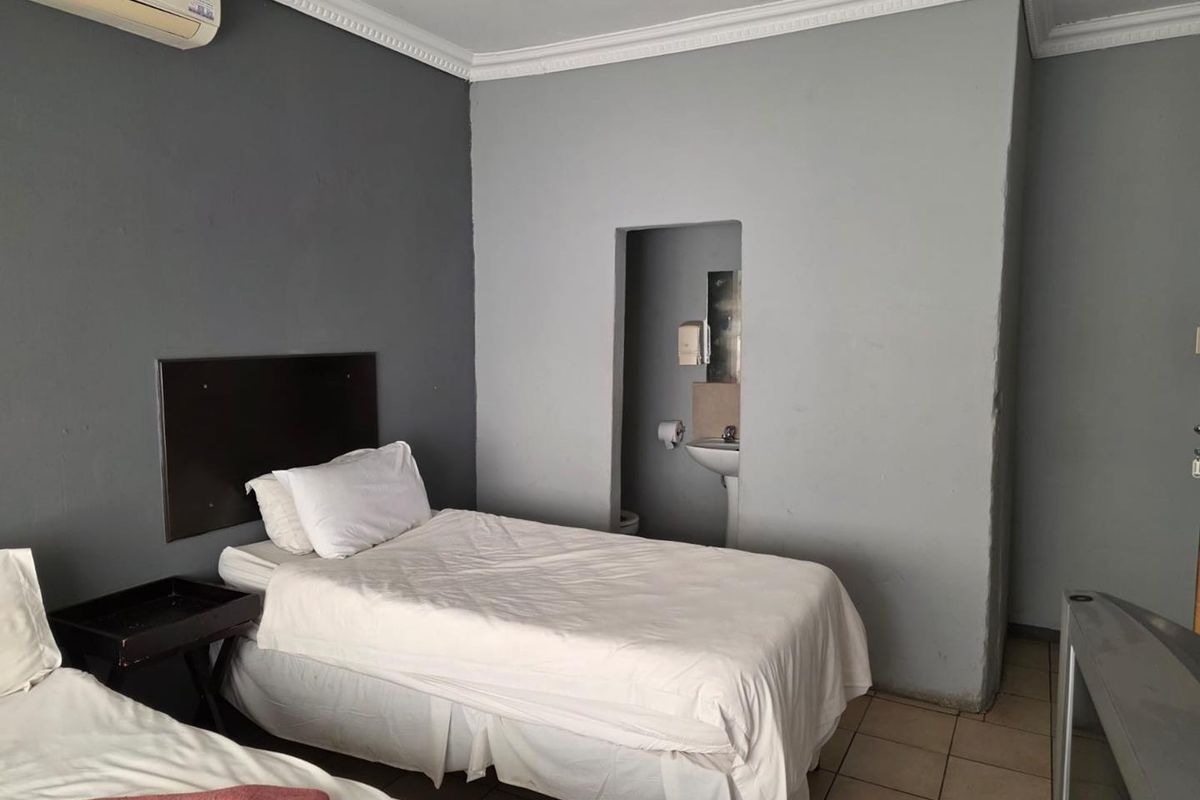 A bedroom featuring a wall-mounted air conditioning unit, tiled flooring, and an integrated en-suite bathroom area with a pedestal basin.