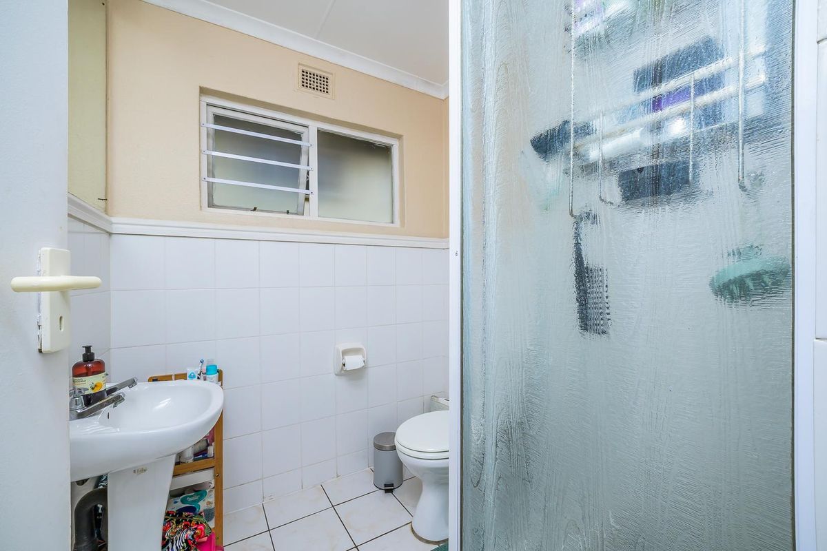 A functional bathroom featuring a pedestal basin, a toilet, and a shower enclosure with textured glass doors.