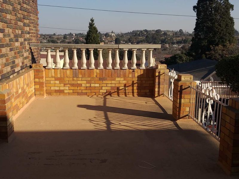 An elevated outdoor balcony featuring brick pillars, a decorative balustrade, and wrought iron railings, offering expansive views of the surrounding area.