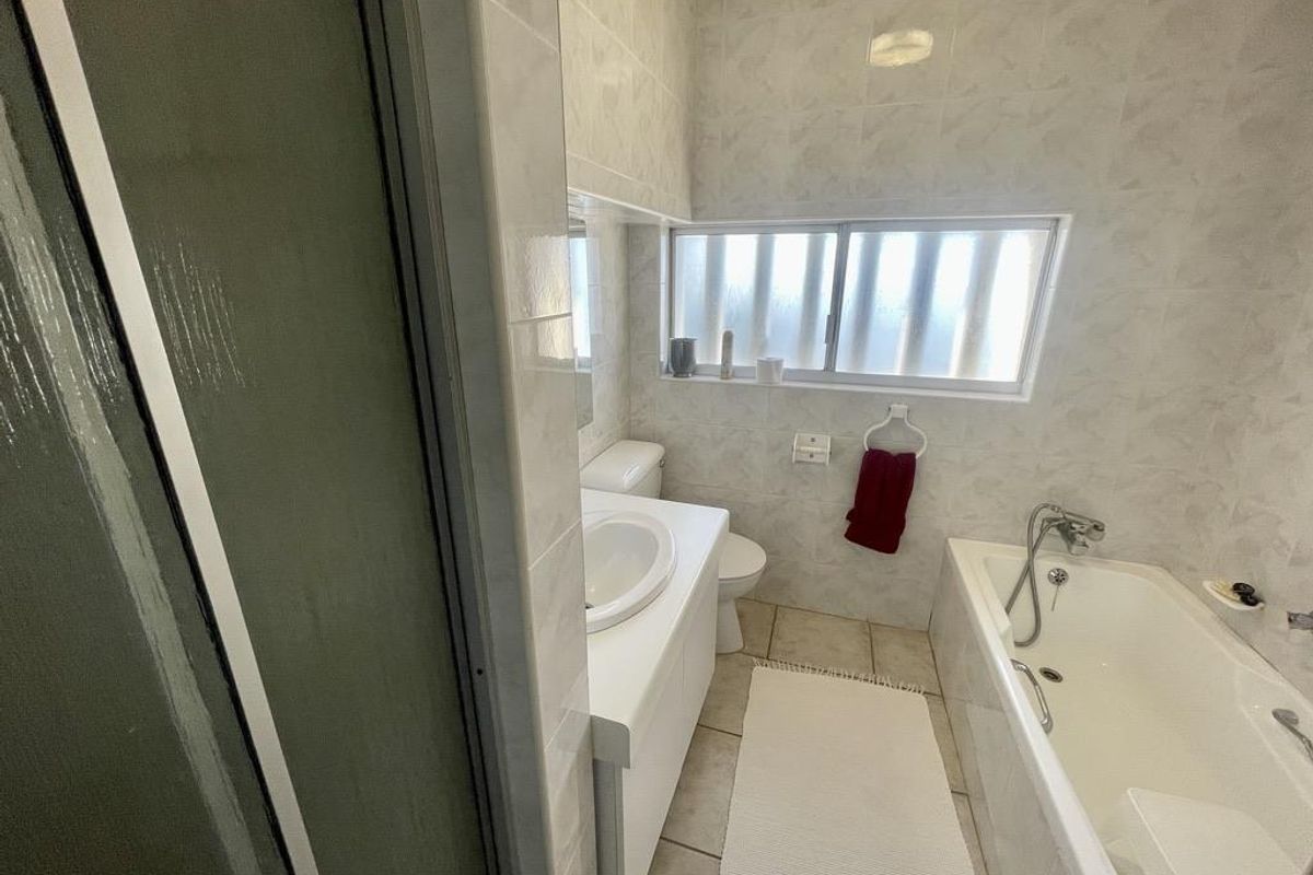 A functional bathroom featuring a built-in bathtub, vanity basin, and toilet, finished with neutral wall tiles and a window for natural light.
