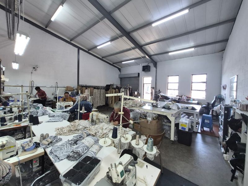 Spacious industrial workshop area featuring high ceilings with exposed steel trusses, concrete flooring, and ample natural light through multiple windows.