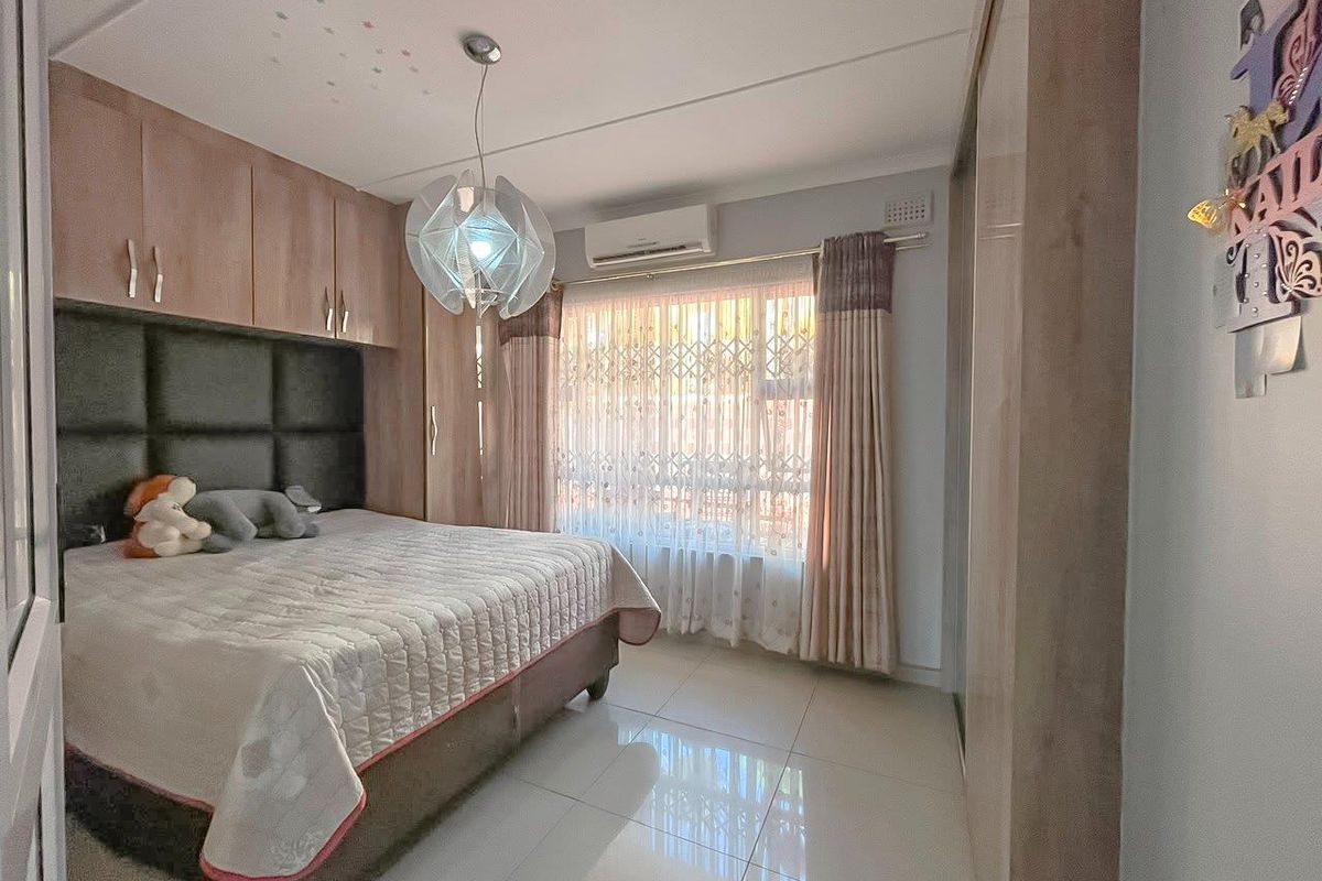 A well-maintained bedroom featuring built-in wooden cabinetry, a wall-mounted air conditioning unit, and tiled flooring.