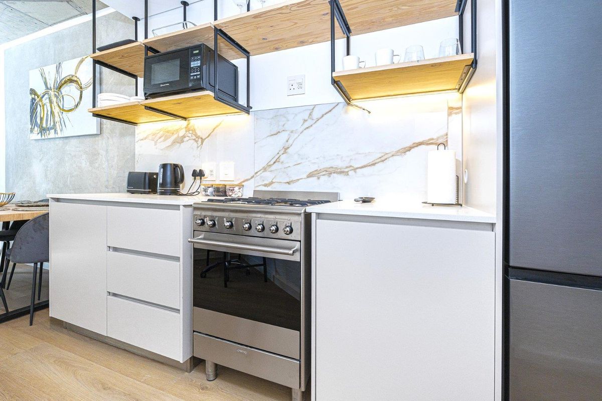 Modern kitchen featuring a gas stove, built-in microwave, marble-look splashback, and stylish open shelving with integrated under-cabinet lighting.