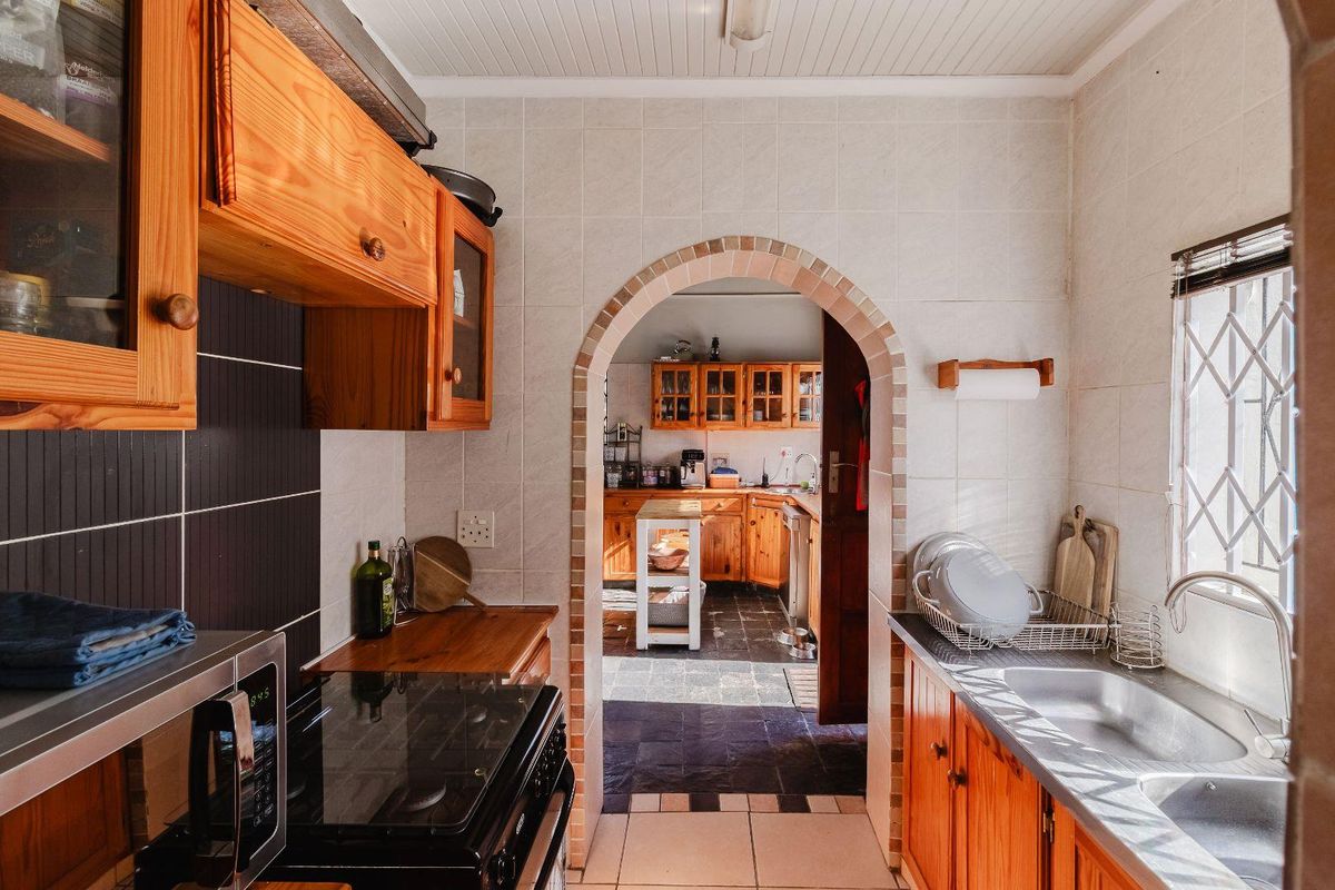 A functional kitchen featuring wooden cabinetry, tiled splashbacks, and a double sink, with an arched doorway leading to an adjacent prep area.