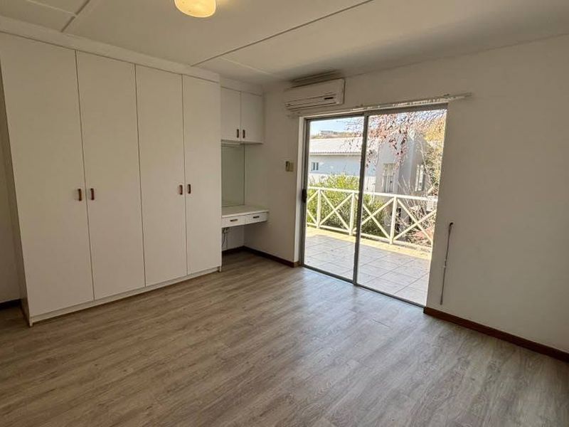 Spacious bedroom featuring built-in cupboards, a vanity area, air conditioning, and direct access to a private balcony through sliding glass doors.