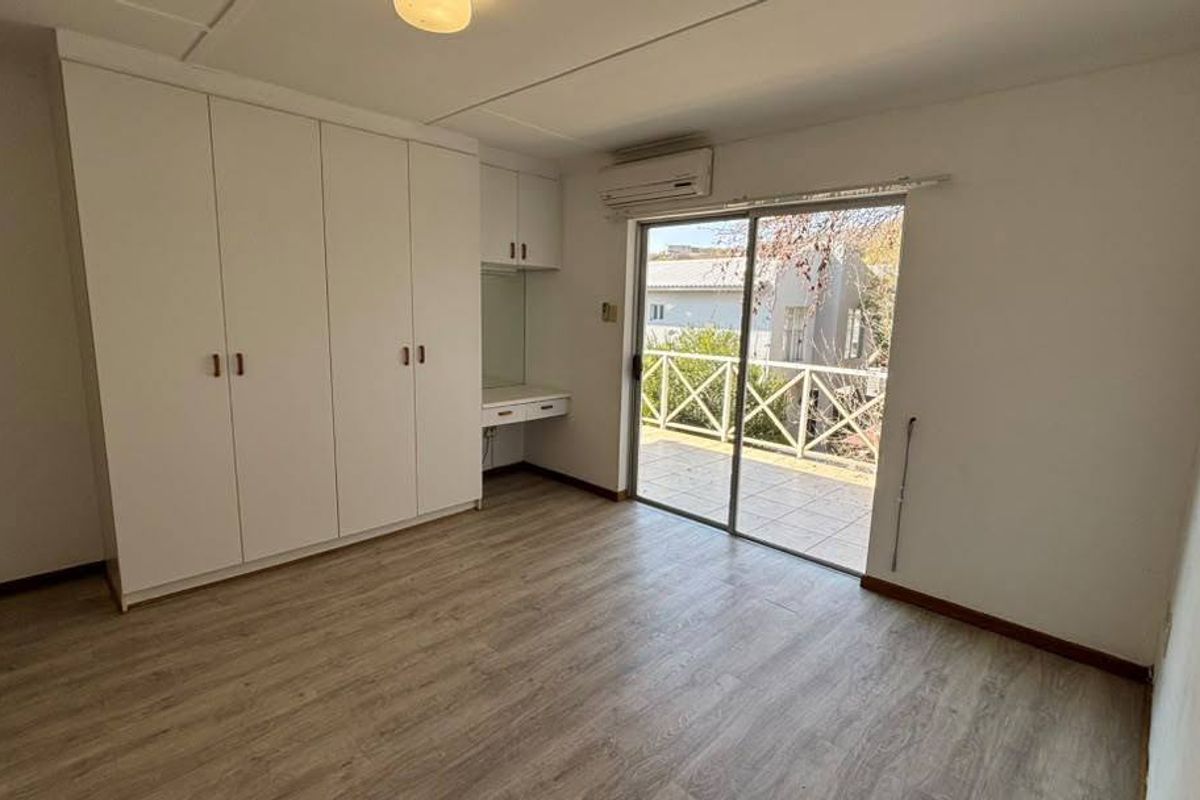 Spacious bedroom featuring built-in cupboards, a vanity area, air conditioning, and direct access to a private balcony through sliding glass doors.