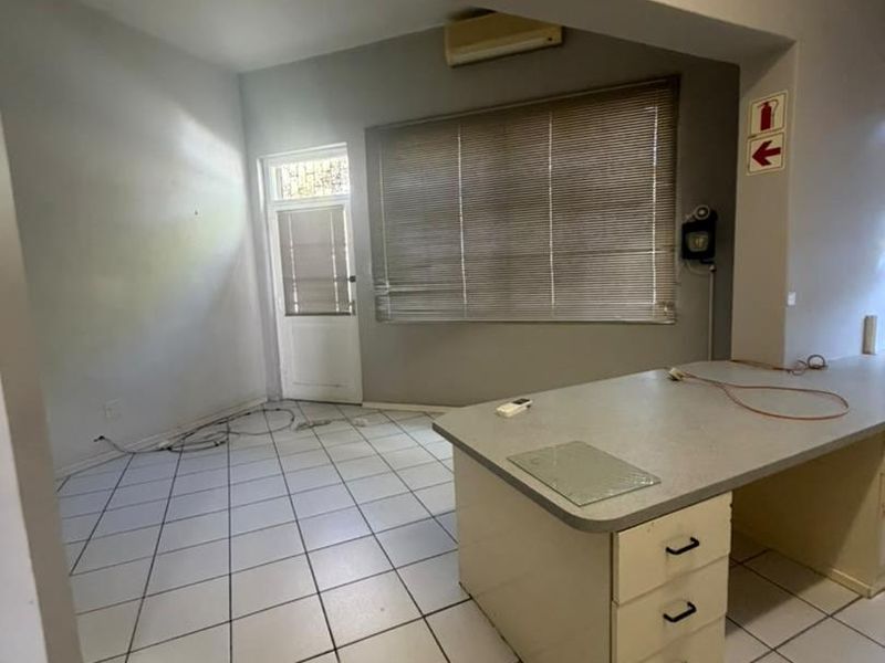 An open-plan space featuring tiled flooring, a built-in desk unit, and a wall-mounted air conditioning unit, suitable for a home office or utility area.