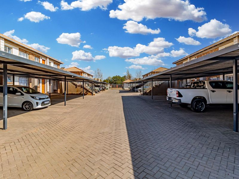 A well-maintained apartment complex parking area featuring covered parking bays and neat brick-paved driveway.