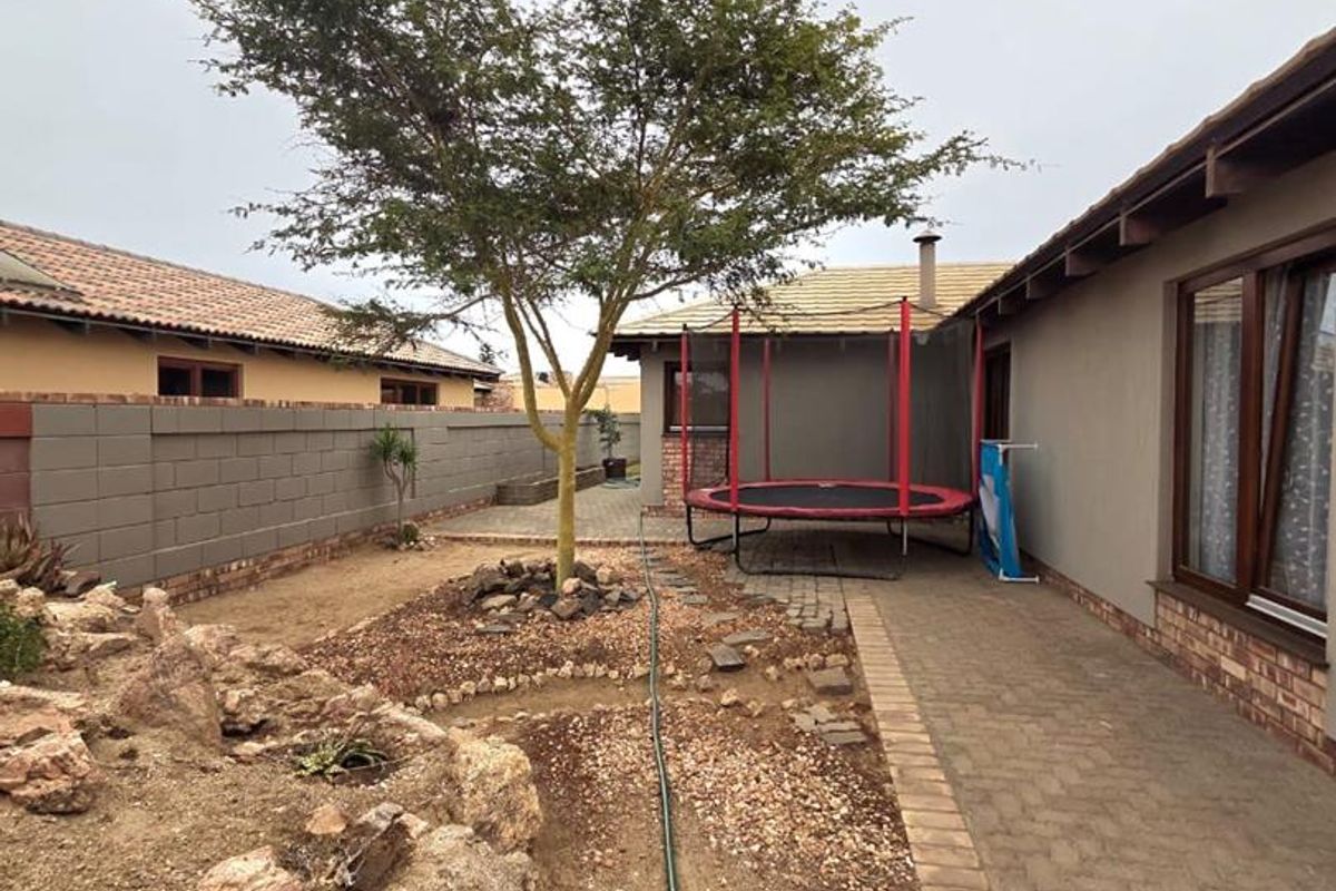 A rear garden area featuring a paved walkway, established tree, rockery, and perimeter walling, providing a functional outdoor space.