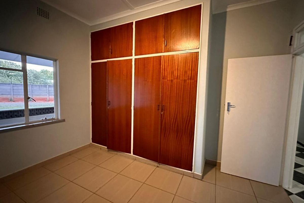 A clean, empty bedroom featuring tiled flooring and ample built-in wooden cupboard storage space.