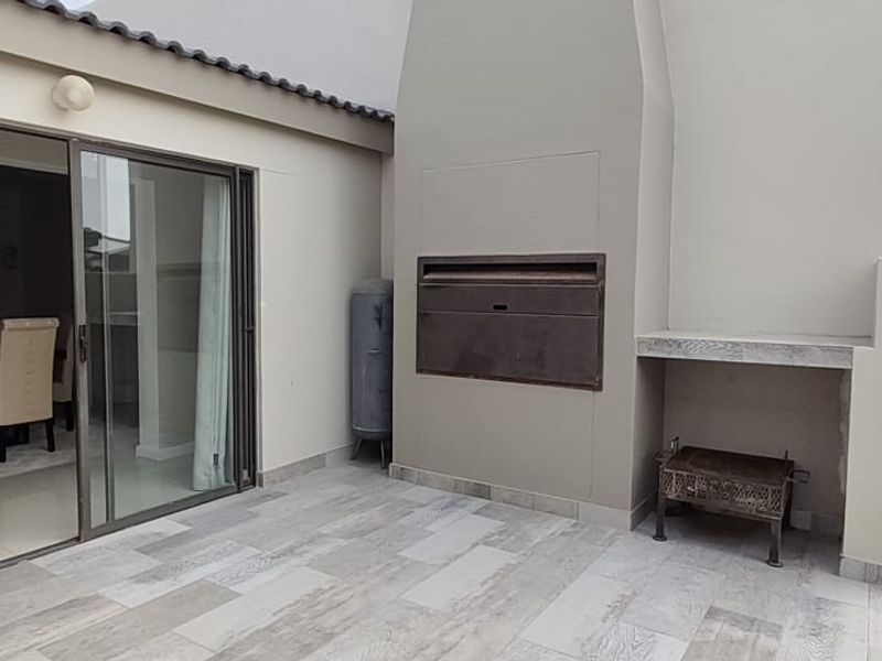 Covered patio area featuring a built-in braai, tiled flooring, and sliding glass doors providing seamless access to the interior living space.
