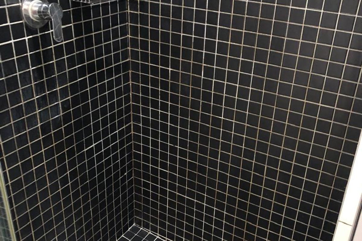 A shower enclosure featuring black mosaic wall and floor tiles, equipped with a chrome shower mixer and integrated storage caddy.