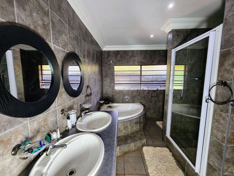 A well-appointed bathroom featuring a double vanity, a raised corner bathtub, and a separate shower enclosure with full-height wall tiling.