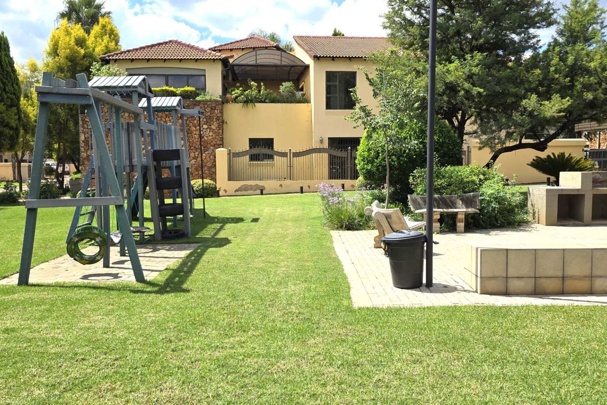 Spacious rear garden featuring a paved patio area with a built-in braai, established lawn, and a children's play structure.