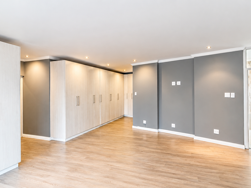 Spacious bedroom featuring extensive built-in cupboards, modern laminate flooring, recessed downlighting, and neutral grey wall finishes.
