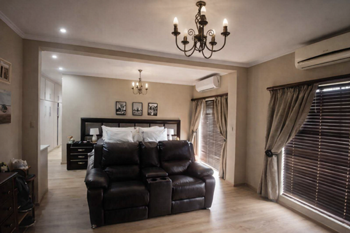 Spacious bedroom featuring light wood-look flooring, dual wall-mounted air conditioning units, and elegant chandelier lighting with integrated storage cabinetry.