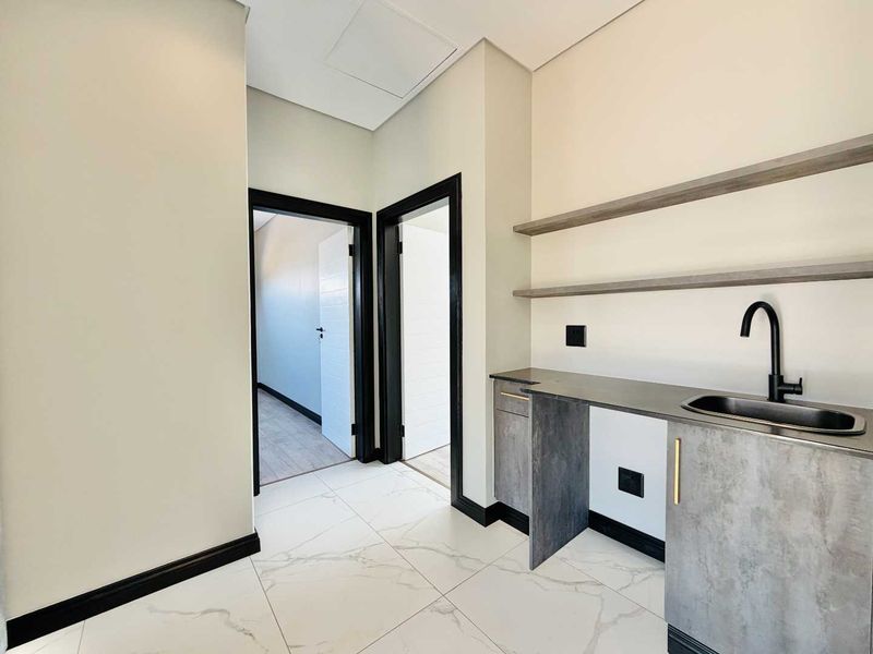 A modern, minimalist scullery or utility area featuring sleek grey cabinetry, a black sink, floating shelves, and polished marble-look floor tiles.