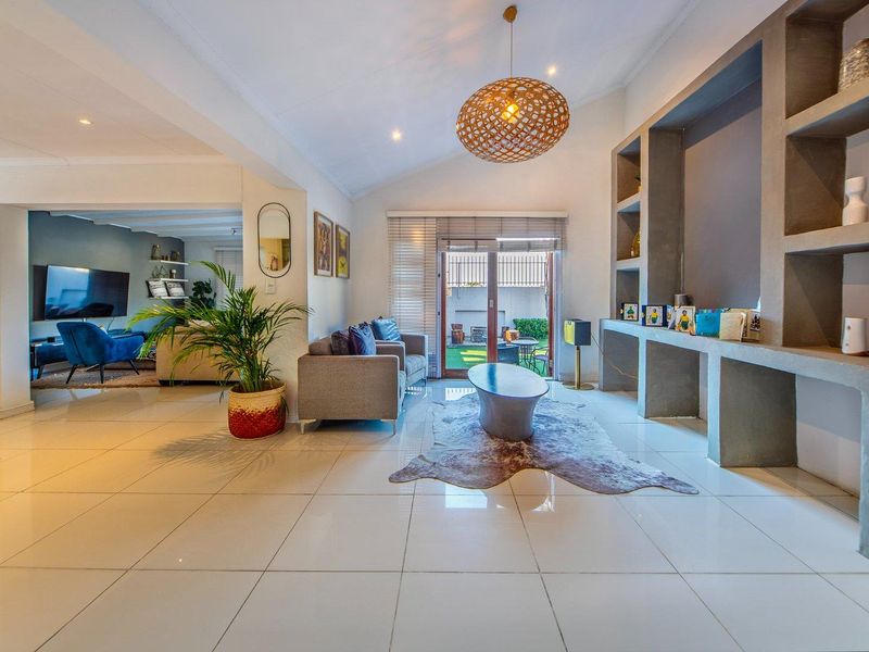Spacious open-plan living area featuring vaulted ceilings, large format floor tiles, and custom built-in shelving, with direct access to the rear patio.