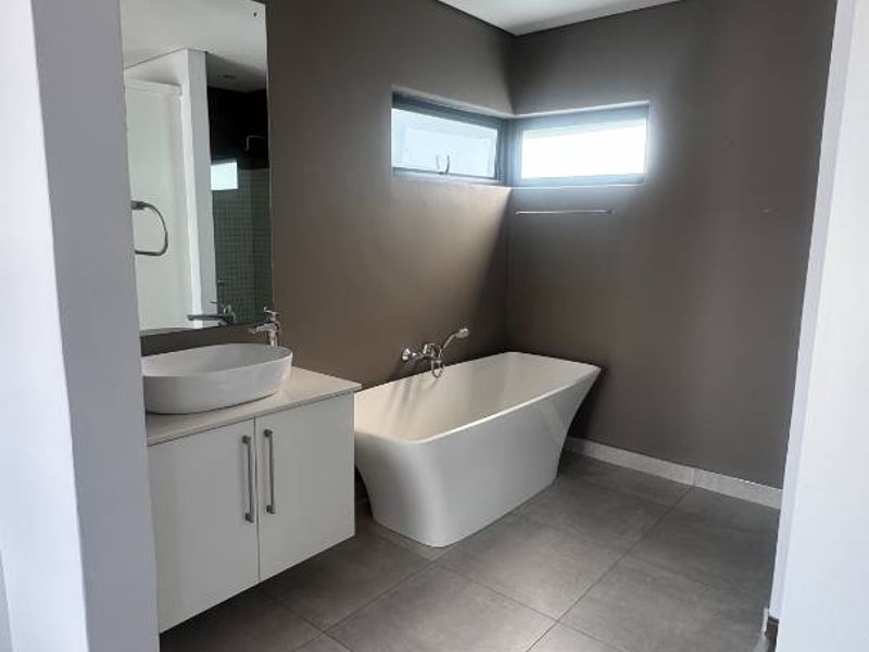Modern bathroom featuring a sleek freestanding bathtub, wall-mounted vanity with vessel sink, and large format floor tiles in a neutral color palette.