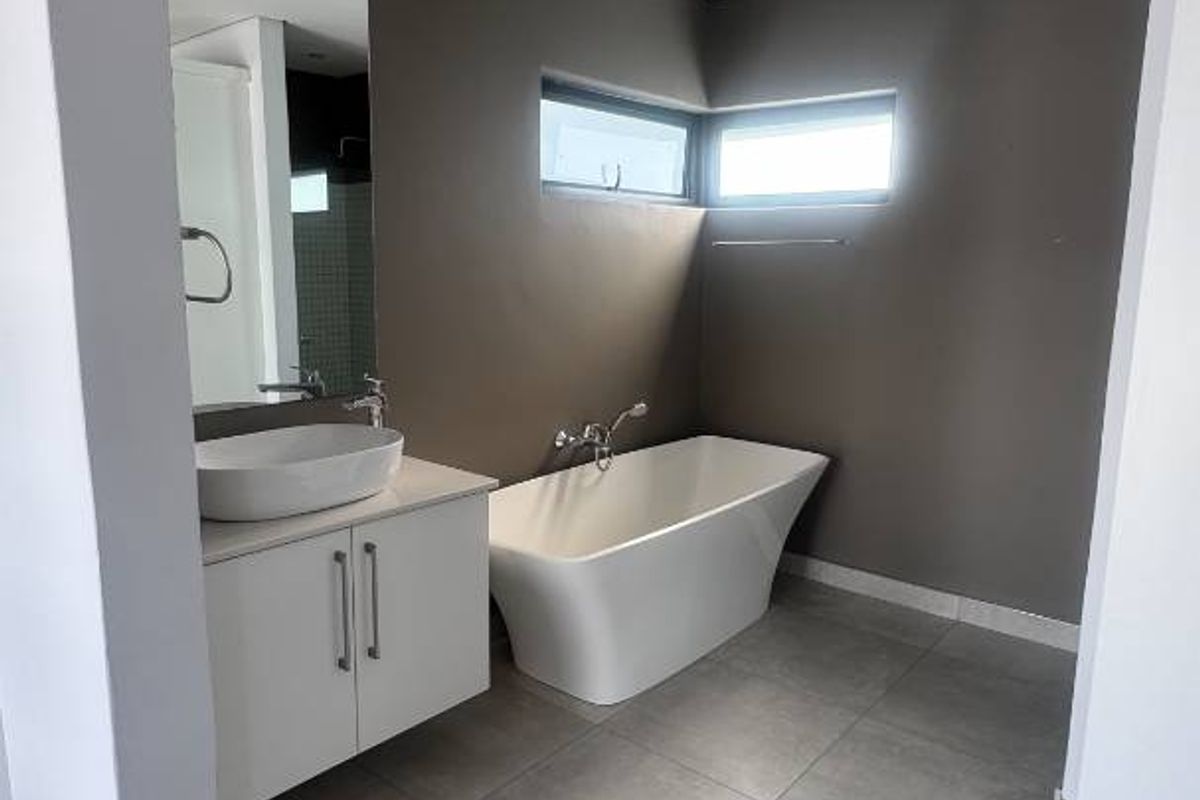 Modern bathroom featuring a sleek freestanding bathtub, wall-mounted vanity with vessel sink, and large format floor tiles in a neutral color palette.