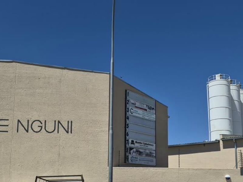 Exterior view of an industrial facility featuring prominent signage, storage silos, and secure perimeter fencing.