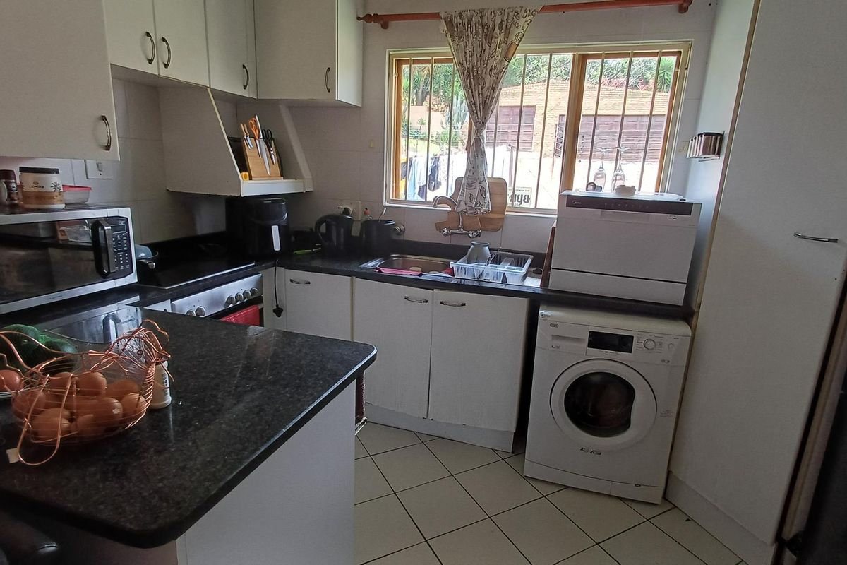 Functional kitchen featuring white cabinetry, dark granite countertops, tiled flooring, and integrated space for laundry appliances under the counter.