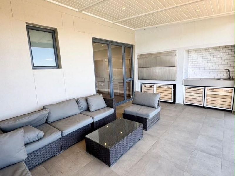 Covered patio featuring a built-in braai, outdoor sink, tiled flooring, and recessed lighting, providing a seamless transition to the interior living space.