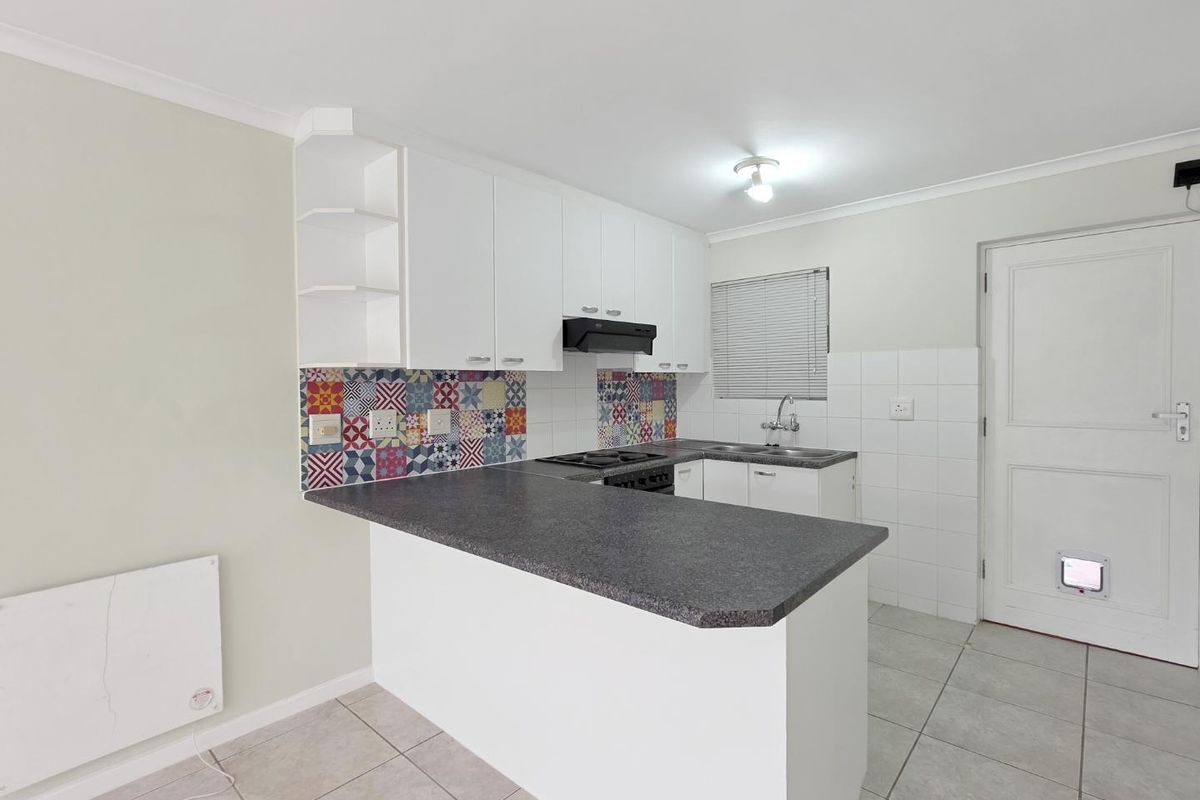 A clean, functional kitchen featuring white cabinetry, a dark laminate breakfast bar, patterned tile backsplash, and tiled flooring.