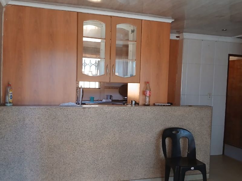 A dated kitchen area featuring built-in wooden cabinetry, a stone-look breakfast bar, and tiled splashbacks, offering potential for a modern renovation.