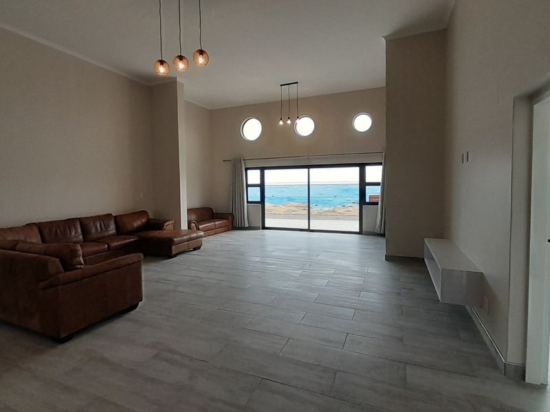 Spacious living area featuring large sliding glass doors with ocean views, modern tile flooring, unique porthole windows, and contemporary pendant lighting.