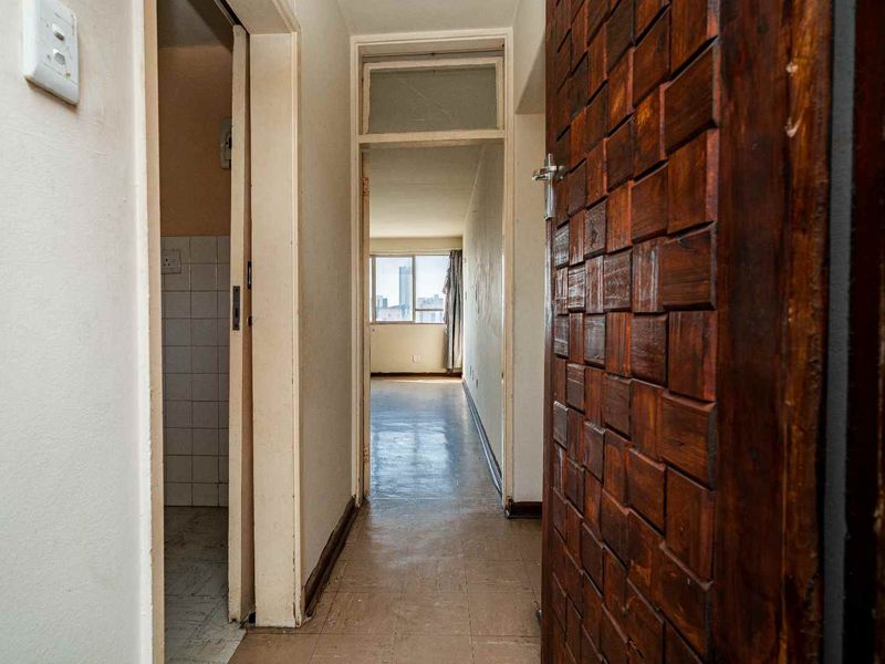 A view through a hallway featuring tiled flooring and a decorative wooden door, leading towards an open living area with natural light.