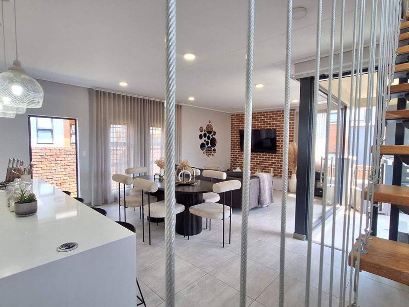 Modern open-plan living area featuring a sleek kitchen island with gas hob, exposed brick accent wall, and a contemporary floating staircase.