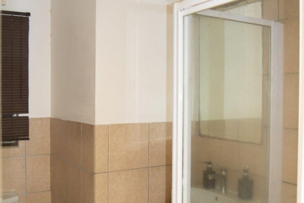 A compact bathroom featuring a shower enclosure, toilet, and vanity basin with neutral wall tiling and basic lighting fixtures.