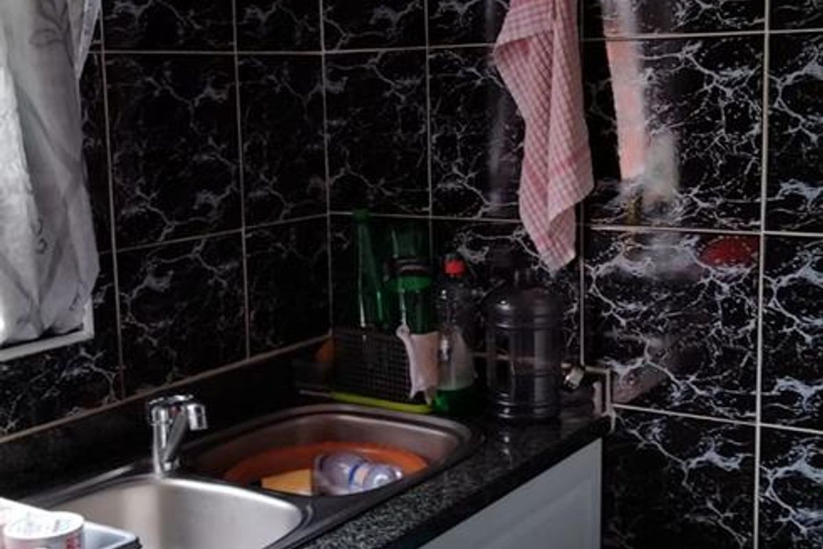 A compact kitchen area featuring a stainless steel sink, dark granite-style countertops, and black marble-effect wall tiling.