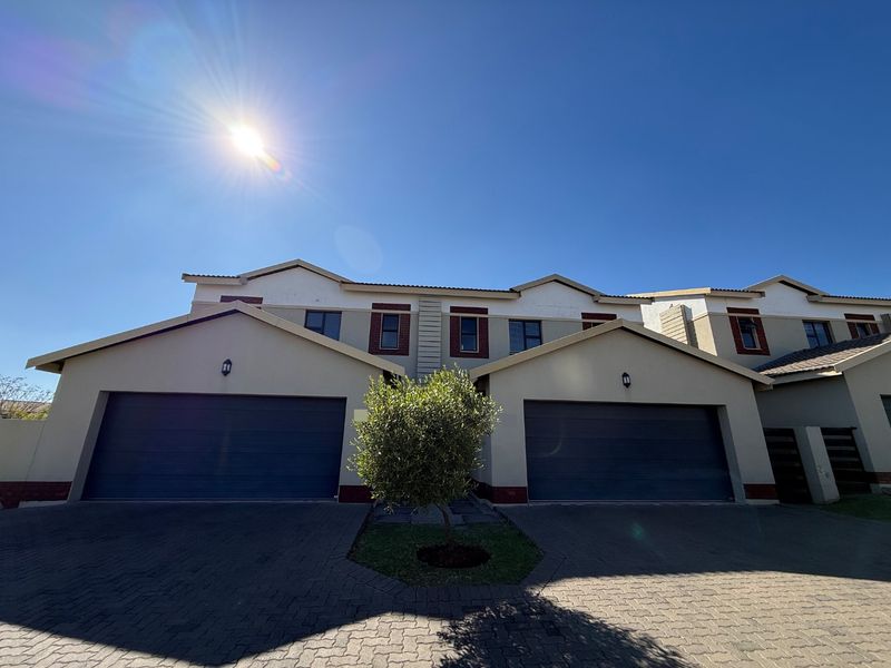 Front elevation of a townhouse complex featuring double garage doors, paved driveway, and well-maintained exterior finishes under a clear sky.