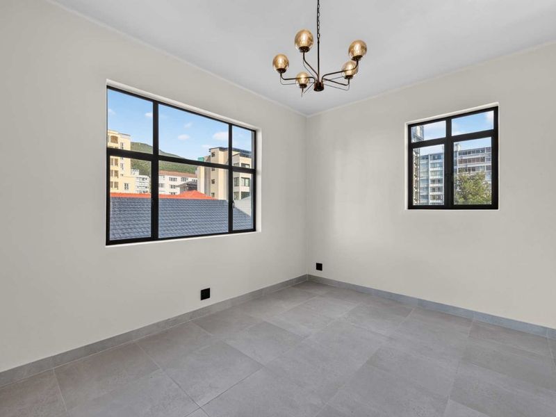 A bright, empty bedroom featuring modern grey floor tiles, black-framed windows, and a contemporary chandelier, offering a clean and neutral space.