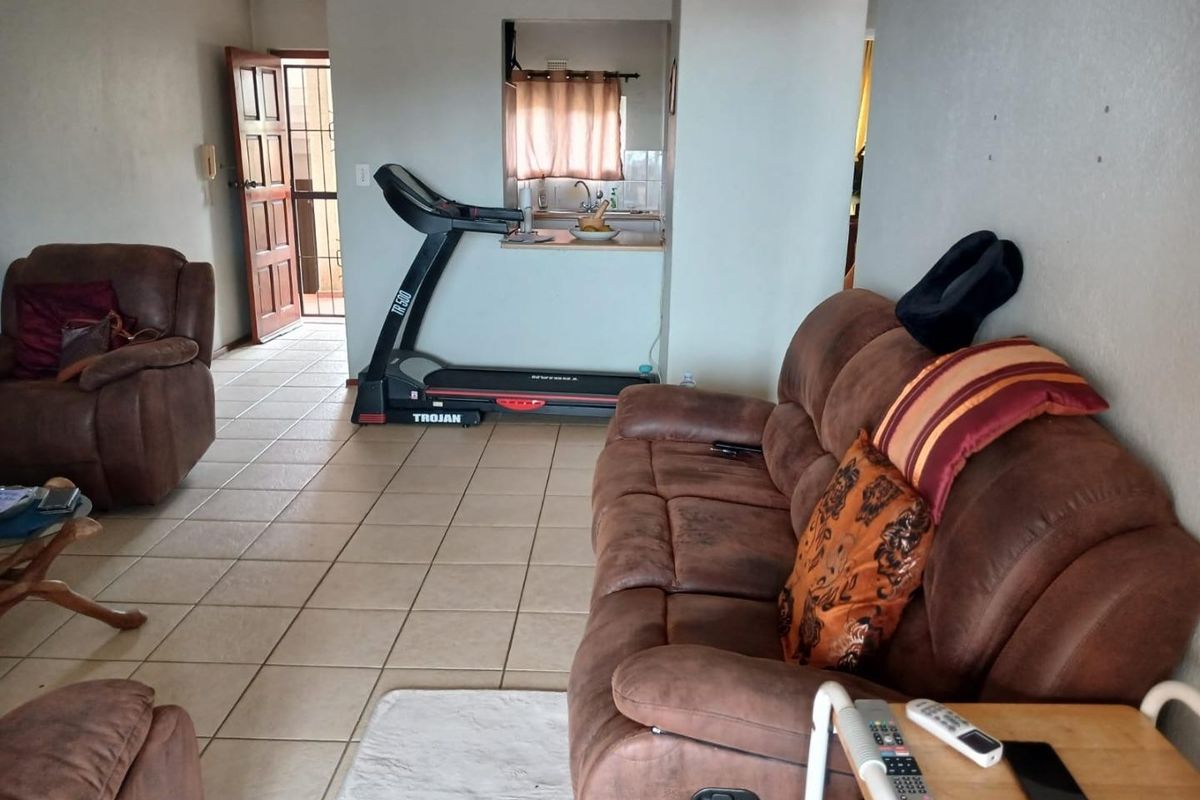 A living room area featuring tiled flooring and a pass-through window connecting to the kitchen, with direct access to an exterior security door.