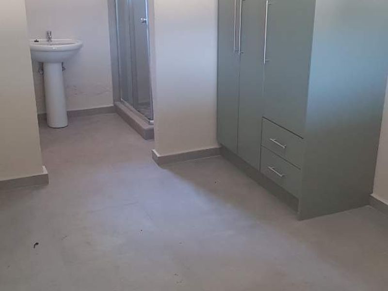A clean, empty bedroom featuring a built-in wardrobe and an en-suite bathroom with a pedestal basin and shower enclosure.