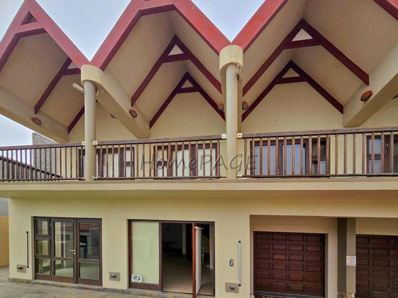 Front elevation of a multi-level home featuring a distinctive pitched roof design, a timber balcony, and a paved driveway with garage access.