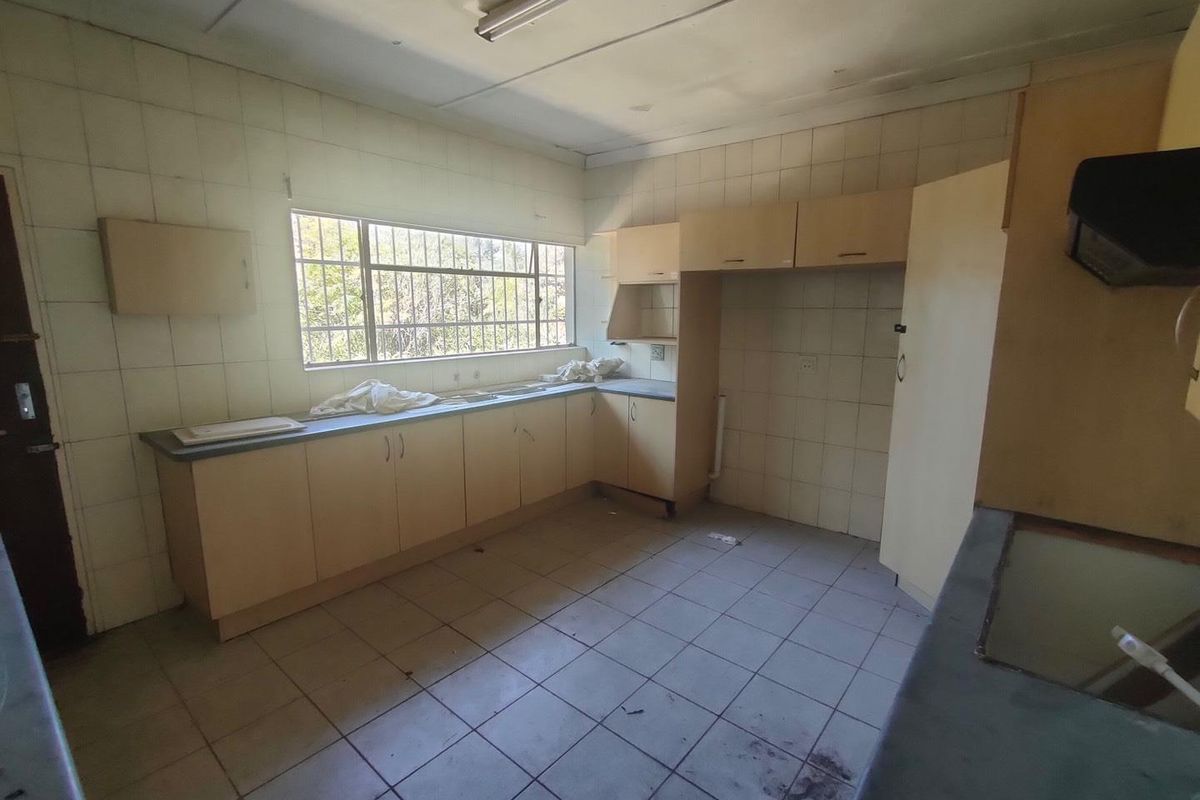 A dated kitchen featuring built-in cabinetry, tiled walls and flooring, and a window with security bars, offering a functional space ready for renovation.
