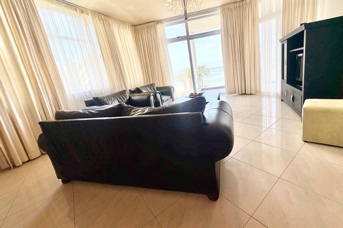 Spacious living area featuring large floor-to-ceiling windows, tiled flooring, and direct access to a balcony with scenic coastal views.