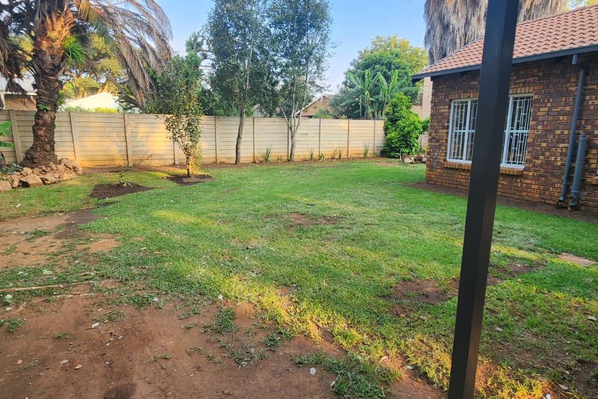 A rear garden view featuring a brick house exterior, security-barred windows, a tiled roof, and a precast concrete boundary wall.