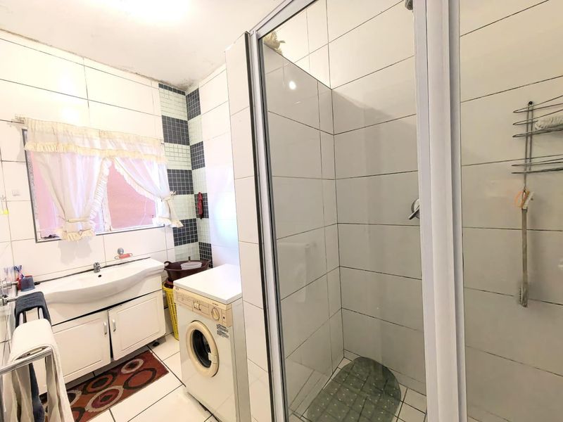 A functional bathroom featuring a vanity basin, a glass-enclosed shower, and tiled finishes, providing essential utility with potential for cosmetic updates.