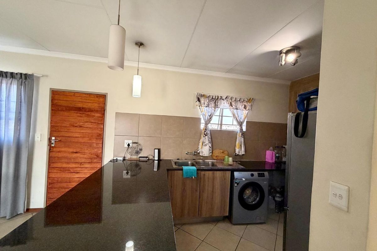 A functional kitchen featuring granite countertops, double basin sink, tiled backsplash, and built-in cabinetry with integrated space for a washing machine.