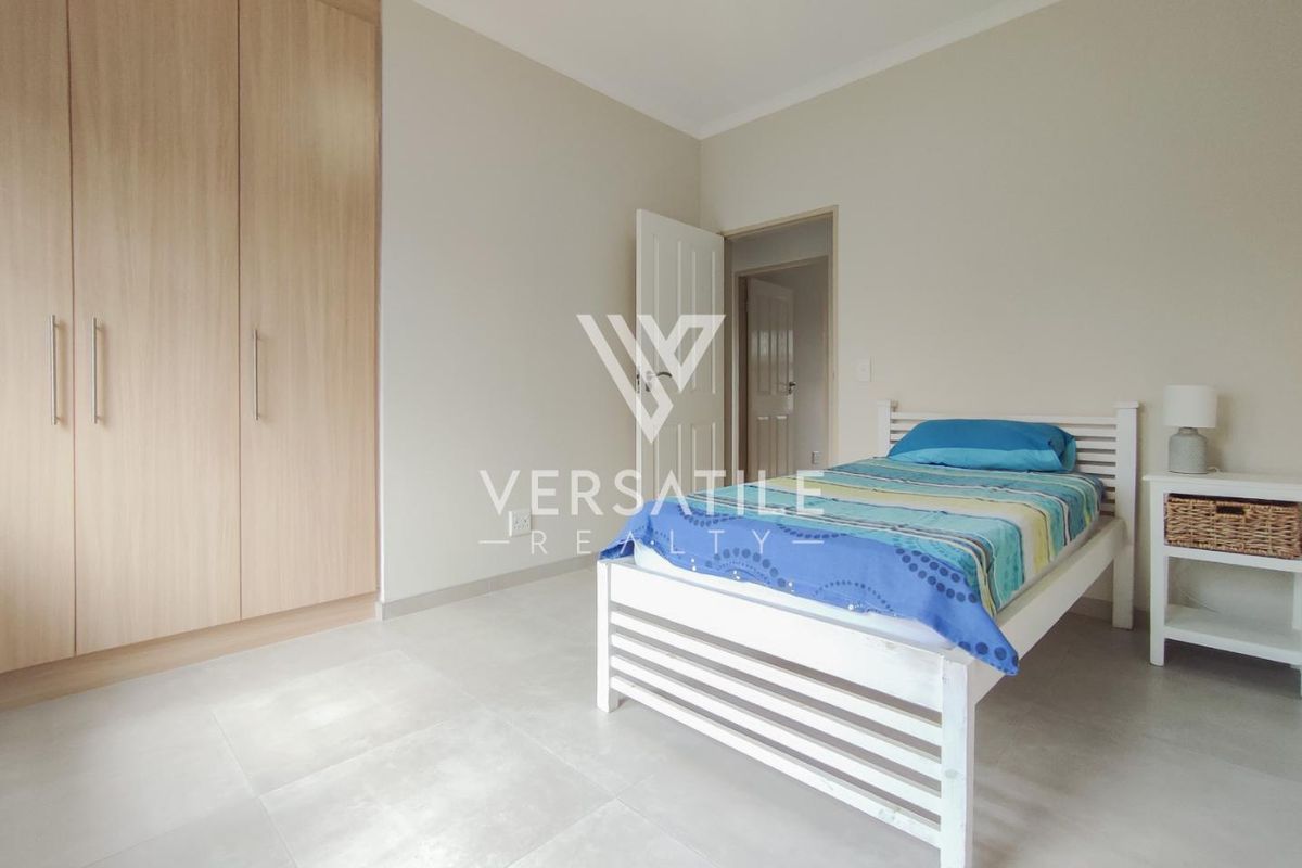 A bright bedroom featuring light-toned floor tiles and built-in wooden cupboards, offering a clean and neutral living space.