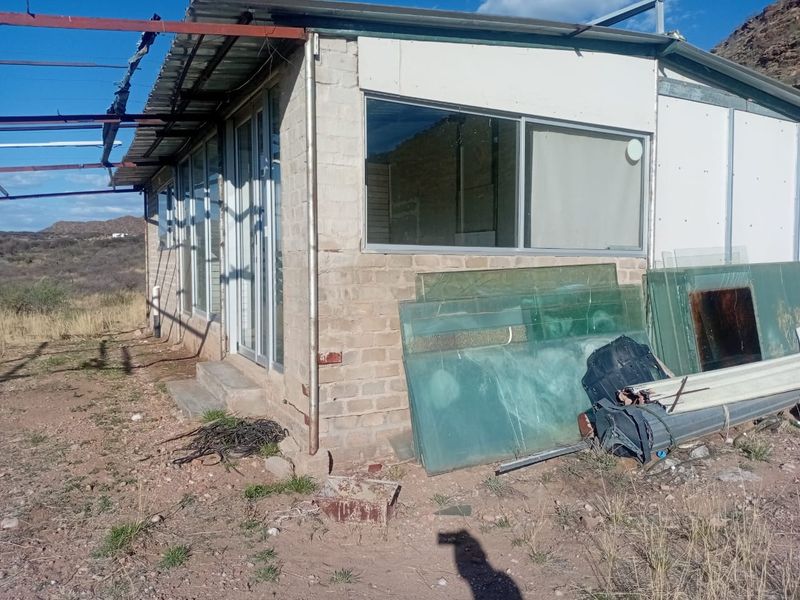 Rear view of a basic brick structure featuring sliding glass doors, aluminum windows, and a metal pergola frame set on agricultural land.