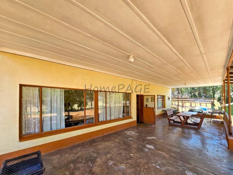 A covered outdoor patio area featuring concrete flooring and timber-framed windows, providing a functional space for outdoor relaxation on this small holding property.